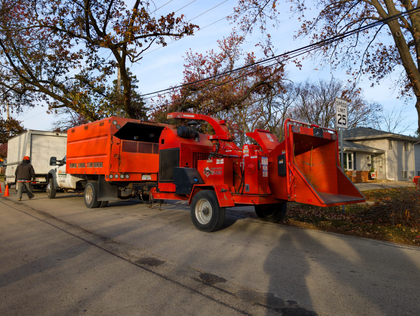 Bright orange wood chipper truck parked on a residential street with workers nearby