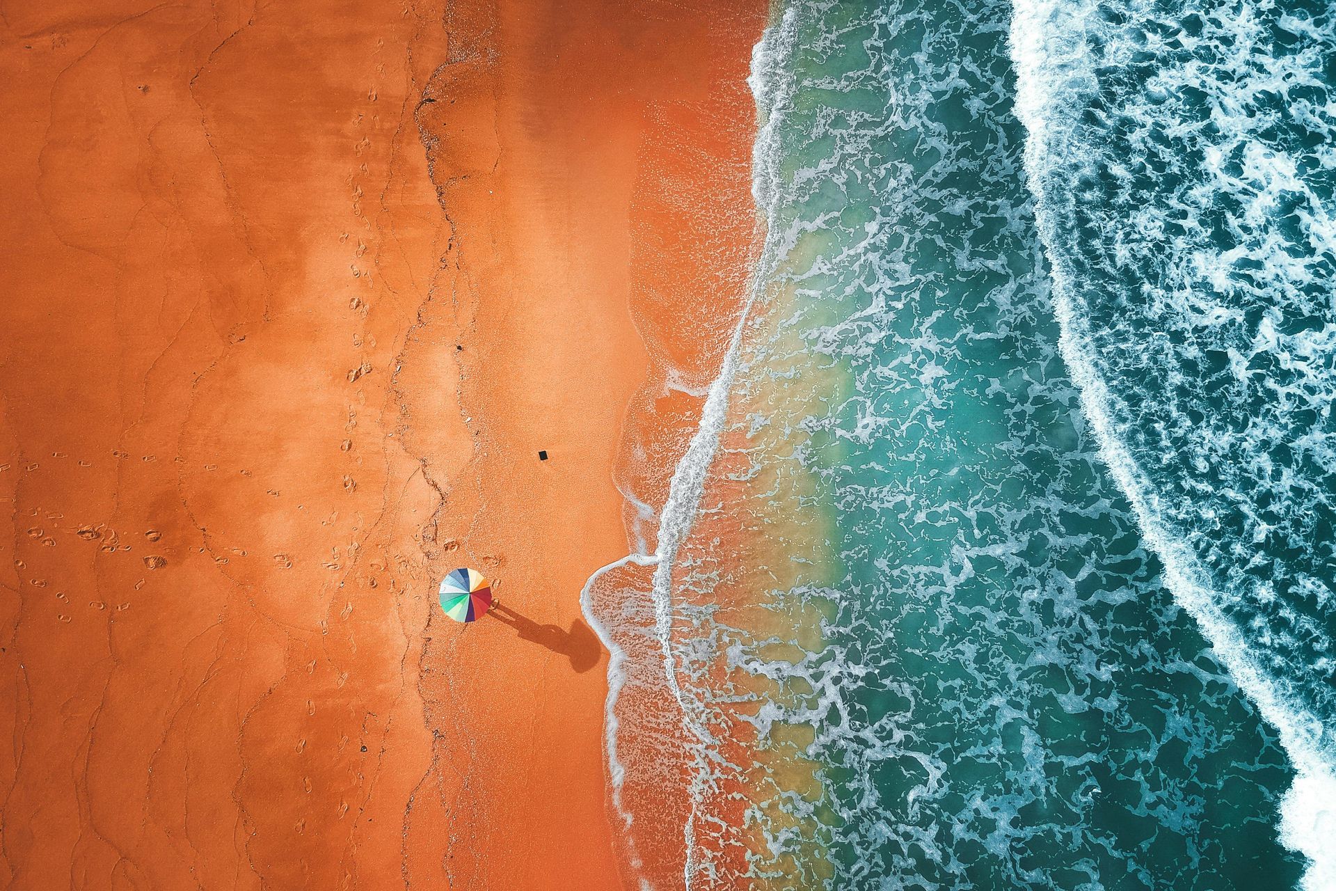 An umbrella on beach with waves coming in from sea
