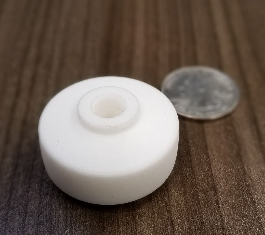 A small white ball is next to a quarter on a wooden table