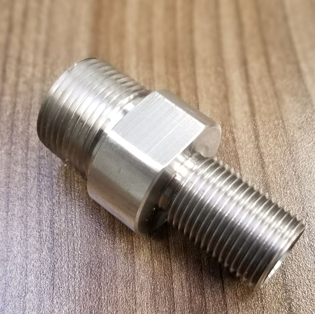 A stainless steel fitting is sitting on a wooden table.