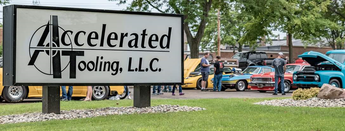 A sign for accelerated tooling llc is in front of a car show.