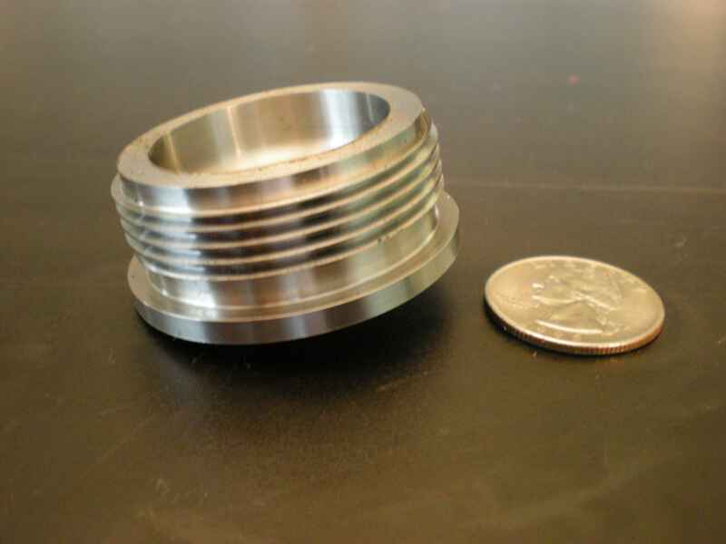 A metal object is next to a quarter on a table.