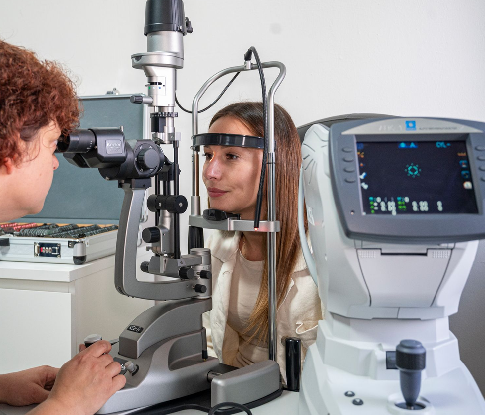 Un paio di occhiali geometrici esposti su uno scaffale rosa in un negozio. Montatura nera con lenti trasparenti e un'immagine promozionale sullo sfondo.