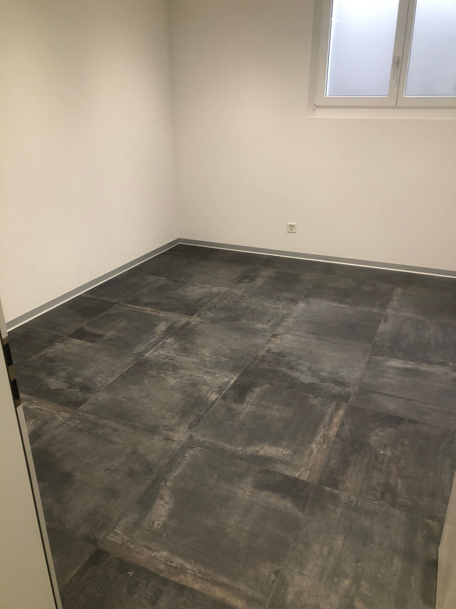 Ein Raum mit grauem Fliesenboden und weißen Wänden.
