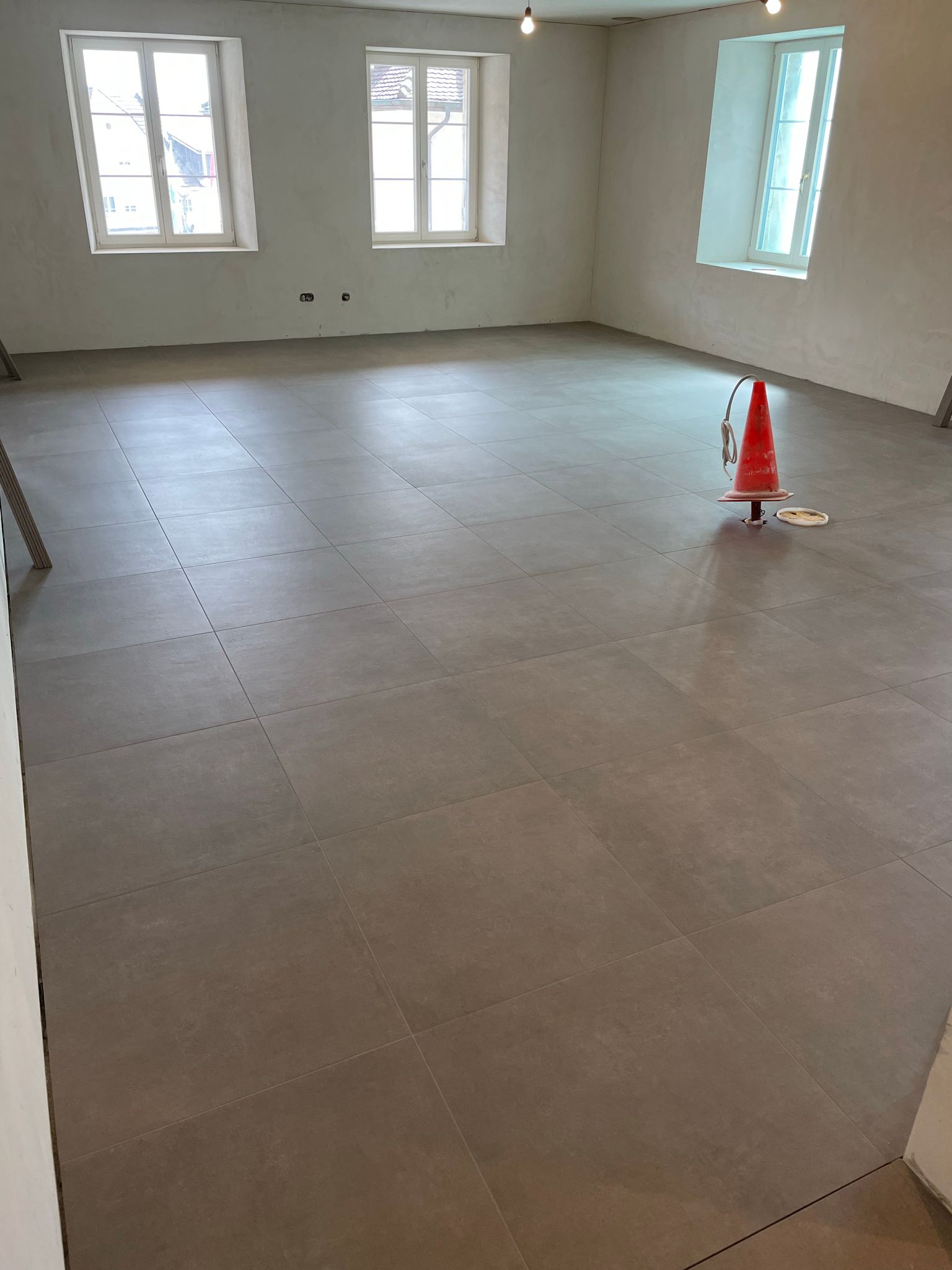 Ein großer Raum mit gefliestem Boden und einem Verkehrskegel auf dem Boden.