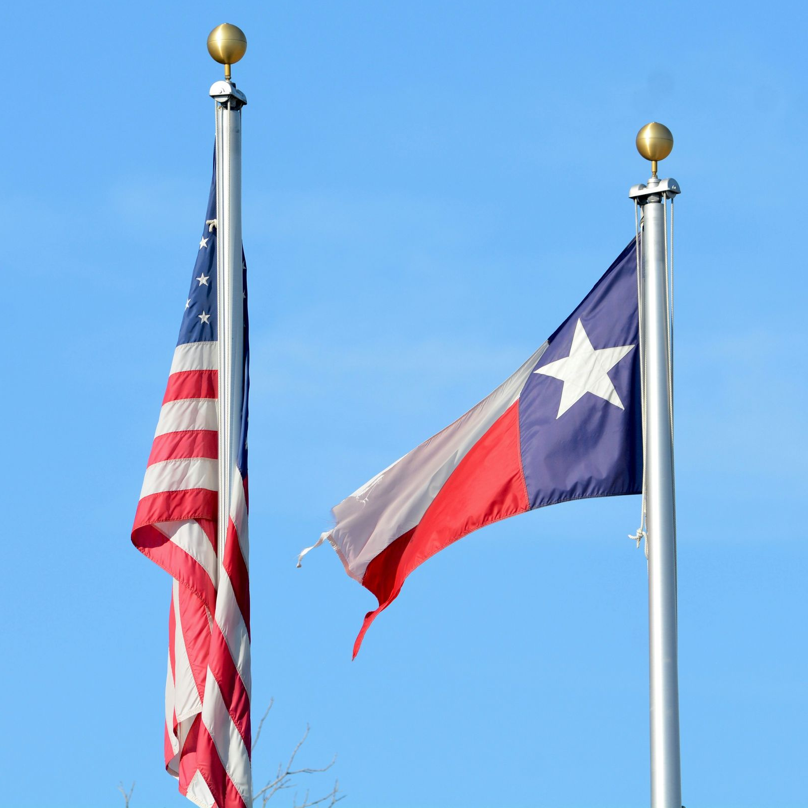 American flag and Texas flag flying on poles against a blue sky.