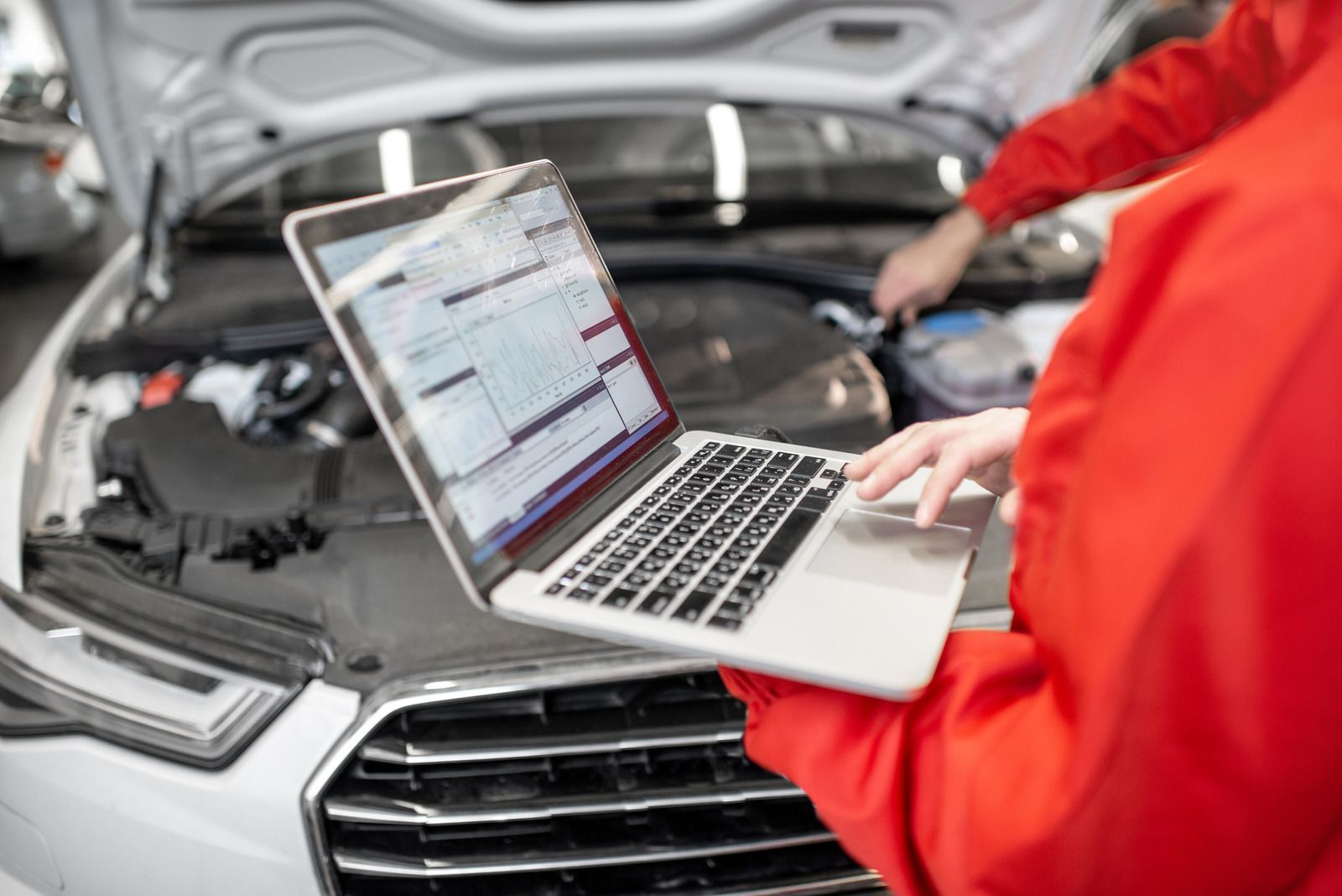 A mechanic is using a laptop computer while working on a car.