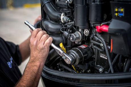 Mechanic using a wrench to work on a black boat engine; close-up shot.