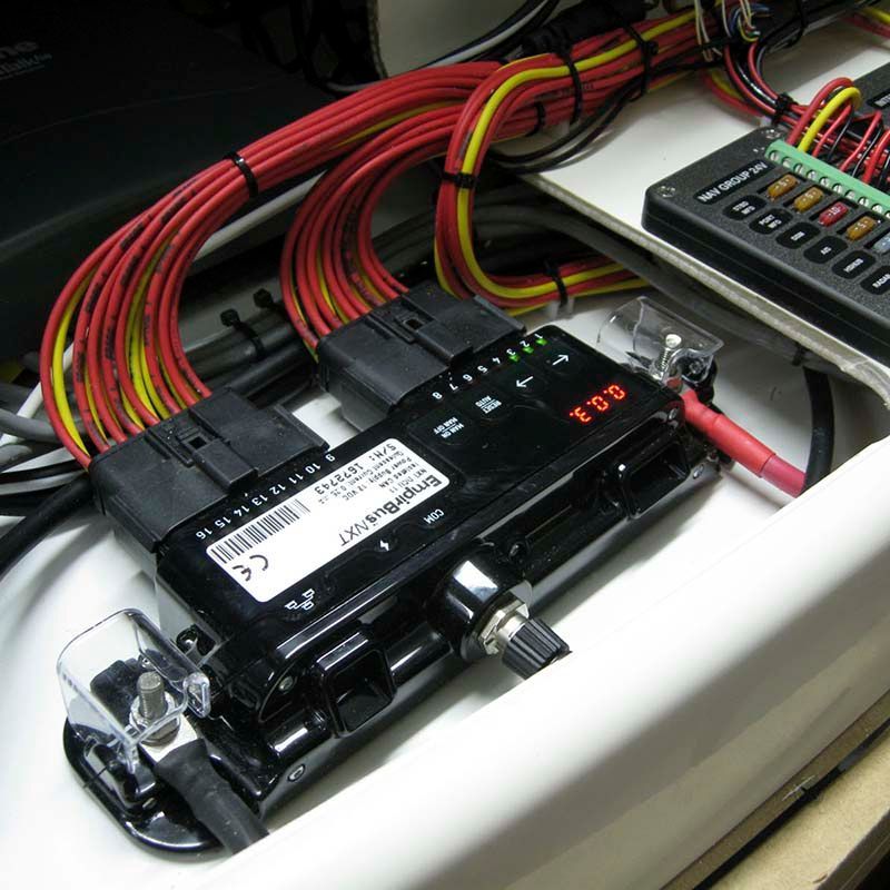 Black electrical component with bundled red and yellow wires. A fuse box is nearby, all in a white compartment.