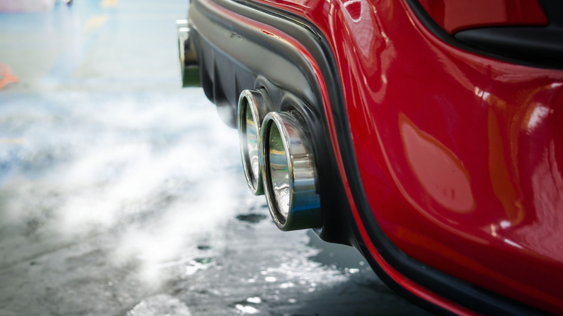 Red car exhaust pipes emitting white vapor.