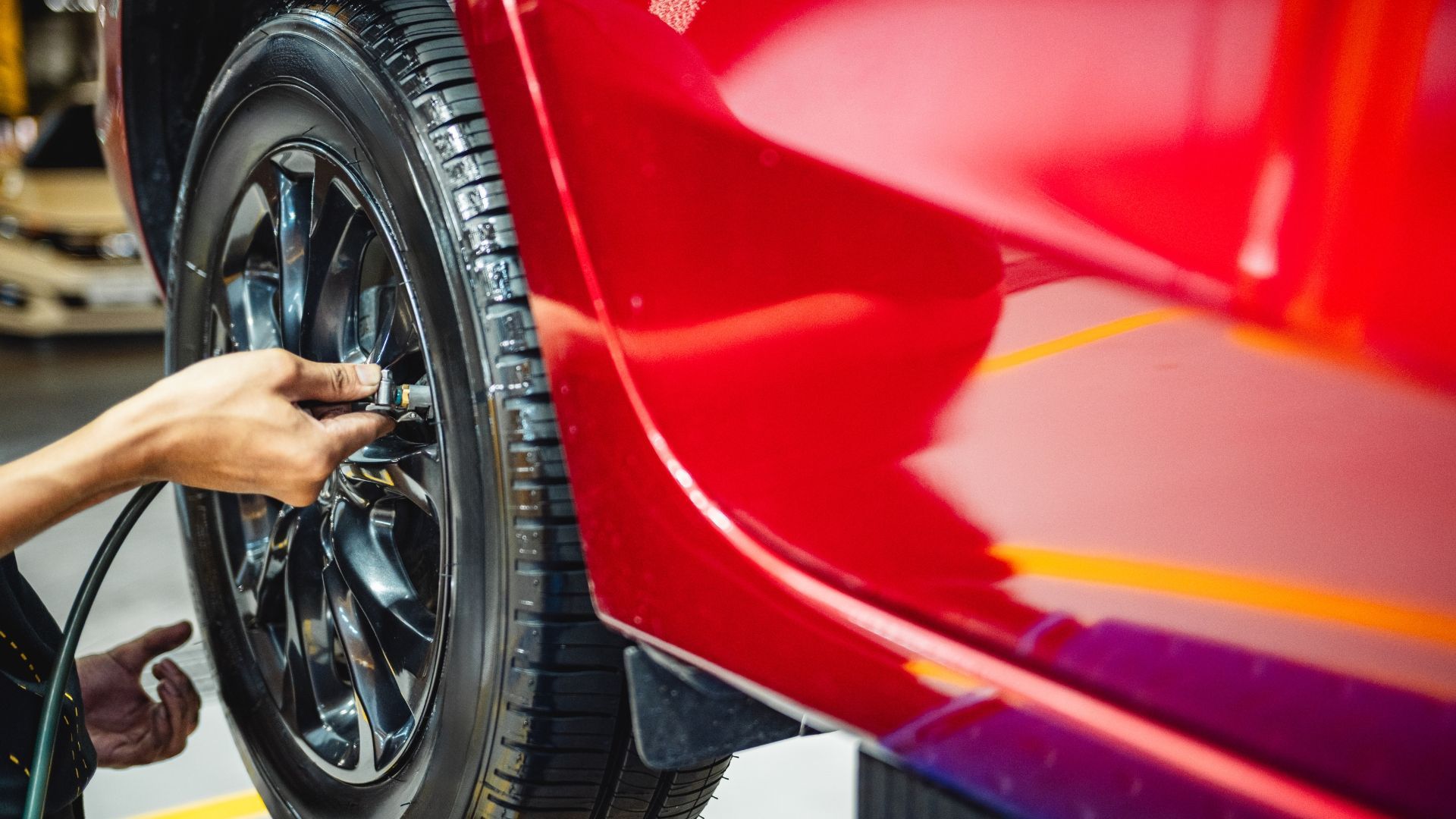 Person inflating a red car tire with a hose in a garage.