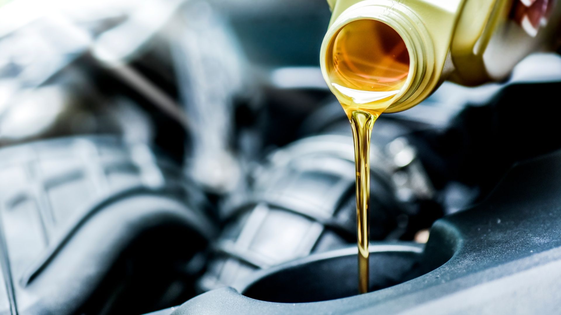Oil being poured from a yellow container into a car engine.