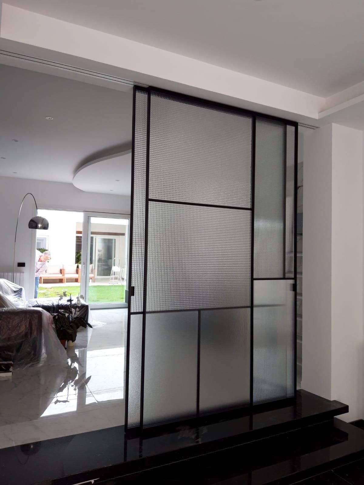 Corridoio con pareti bianche, porte marroni, una porta bianca con pannelli di vetro e uno zerbino.