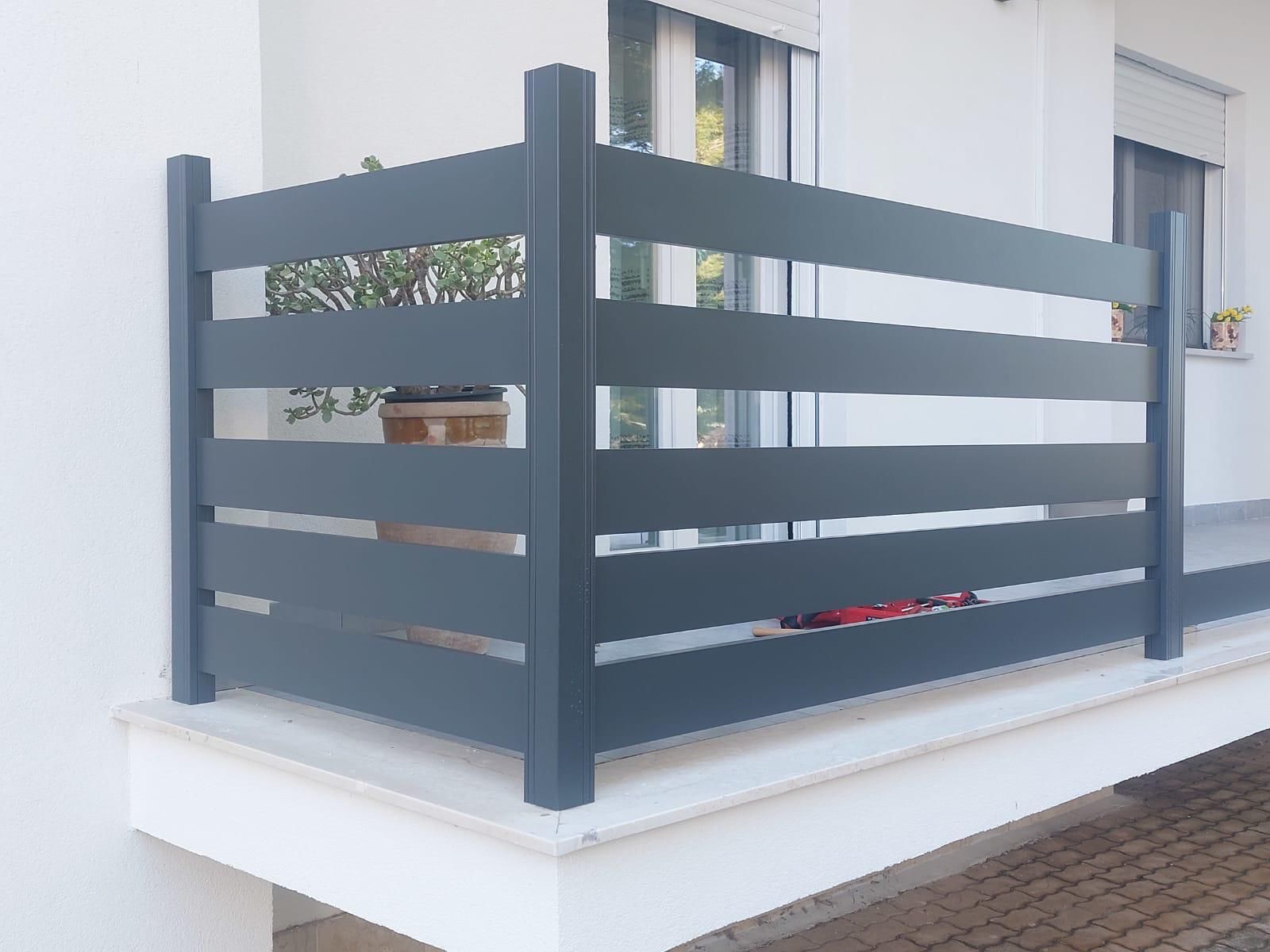 Recinzione in metallo nero in cima a un muro bianco, con rose rosse che crescono accanto; ambiente esterno soleggiato.