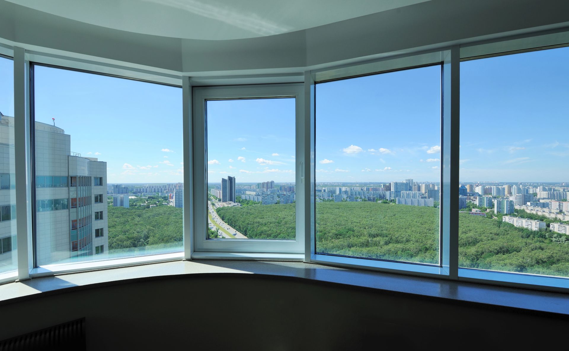 Vista attraverso una grande finestra: paesaggio urbano con cielo azzurro, alberi ed edifici.