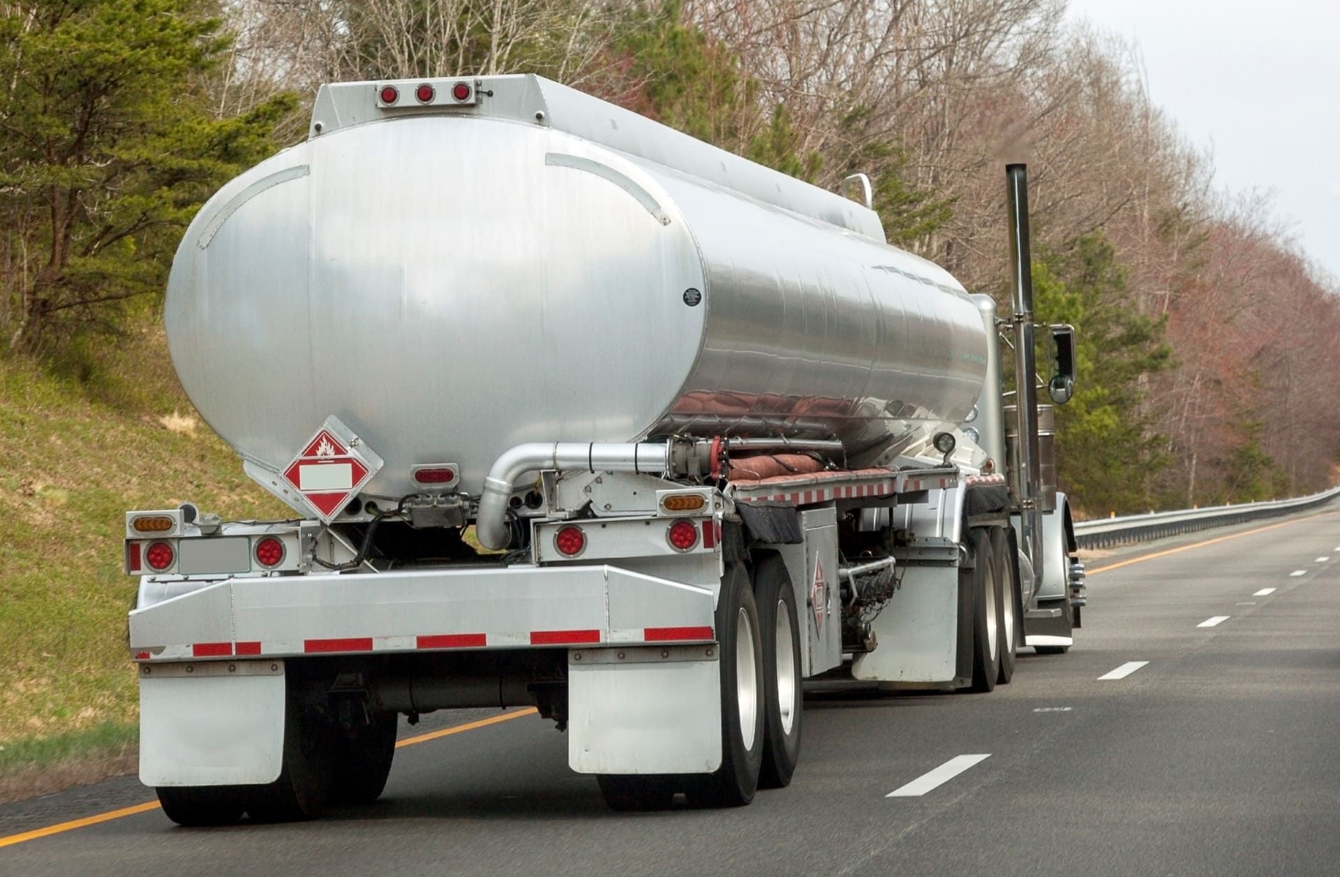 Rear view of fuel truck on highway with trees in background.