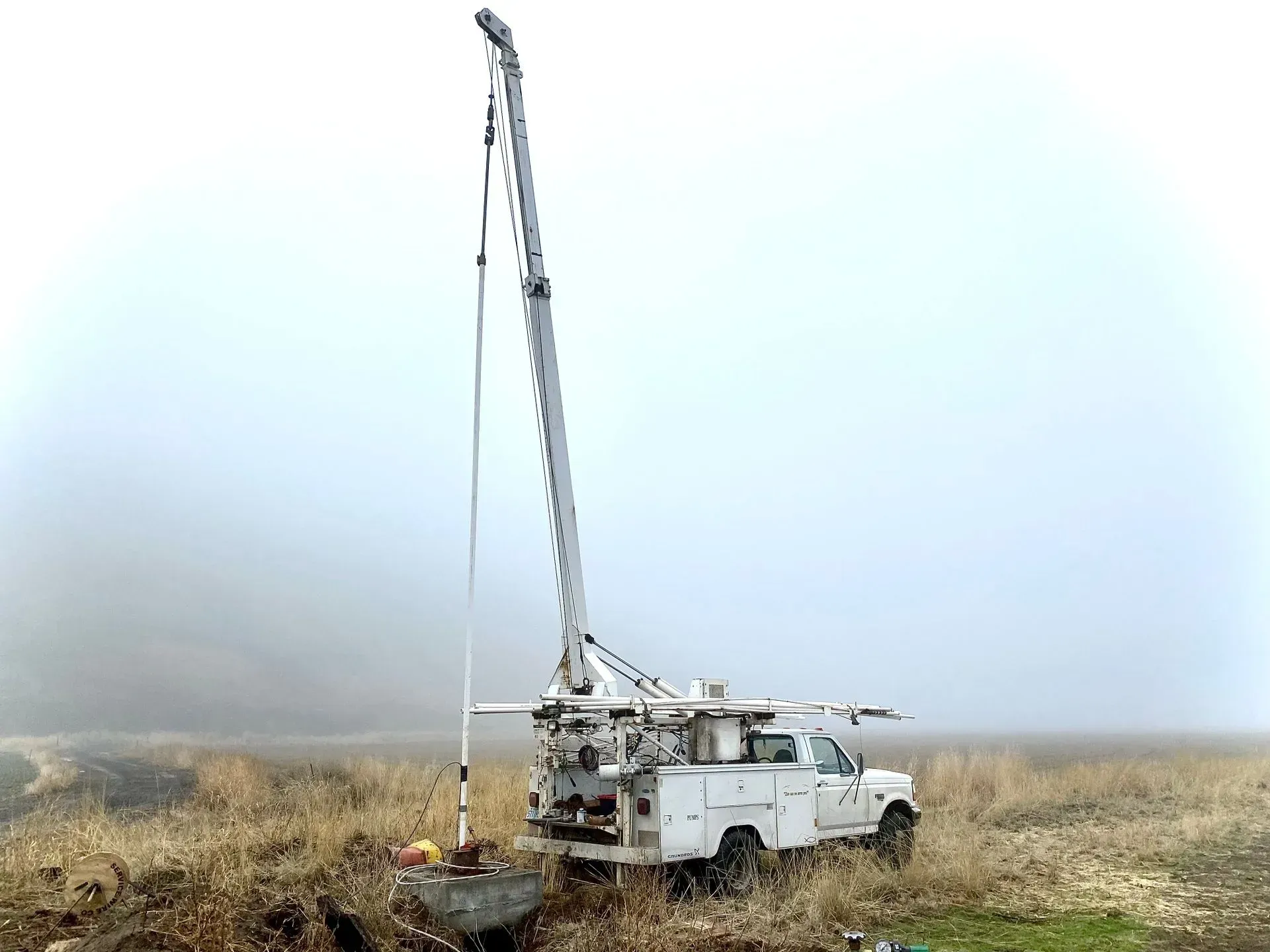 A white truck is parked in a field with a crane attached to it.