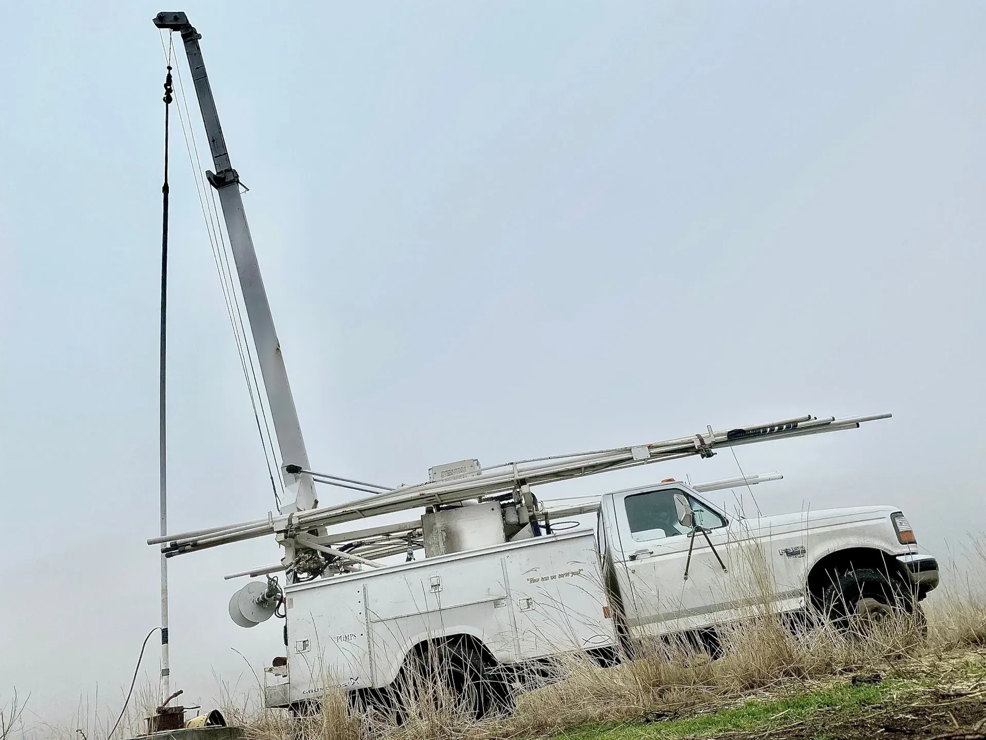A white truck with a crane on the back is parked in a field.