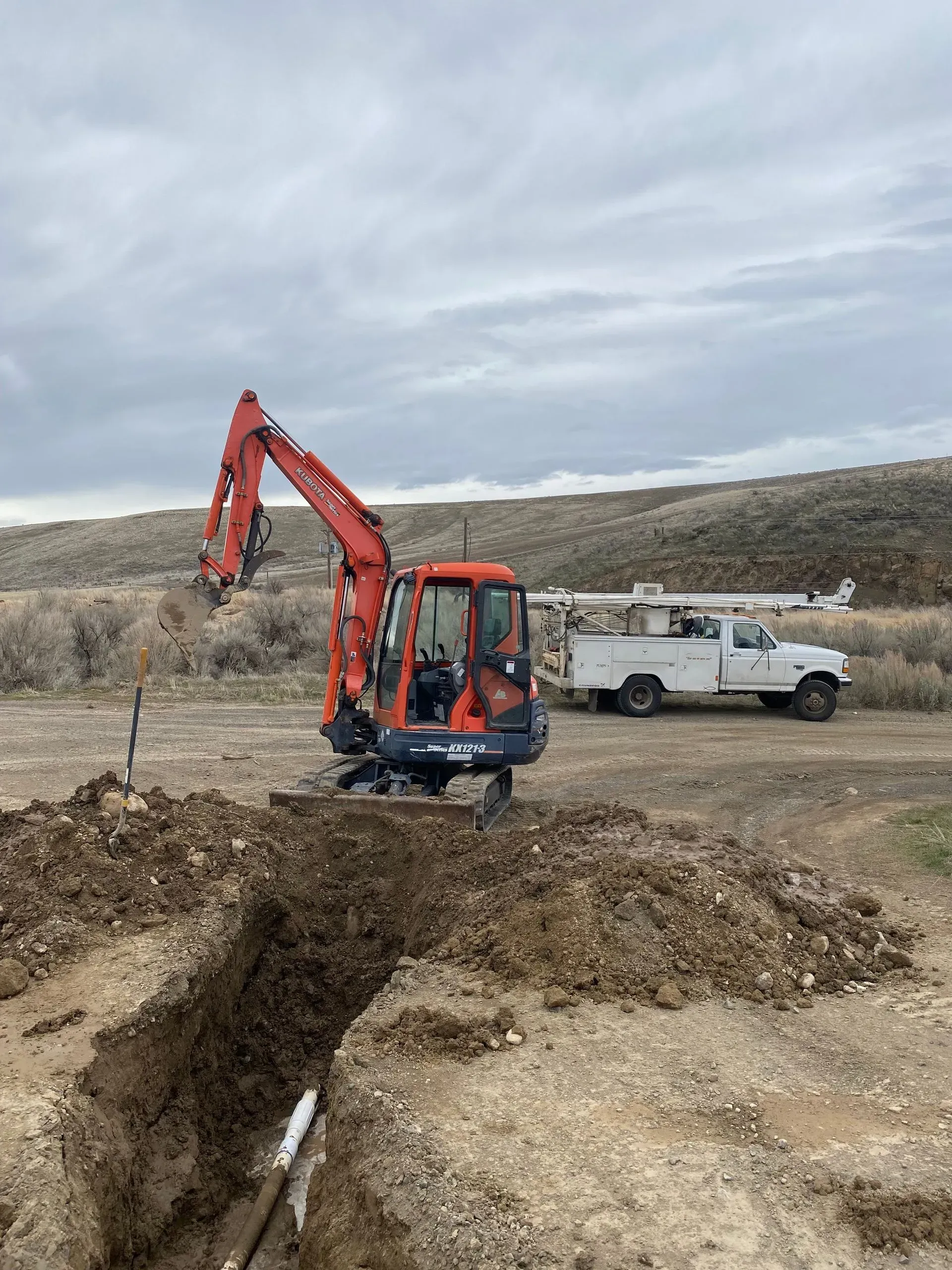 An excavator is digging a hole in the dirt next to a truck.
