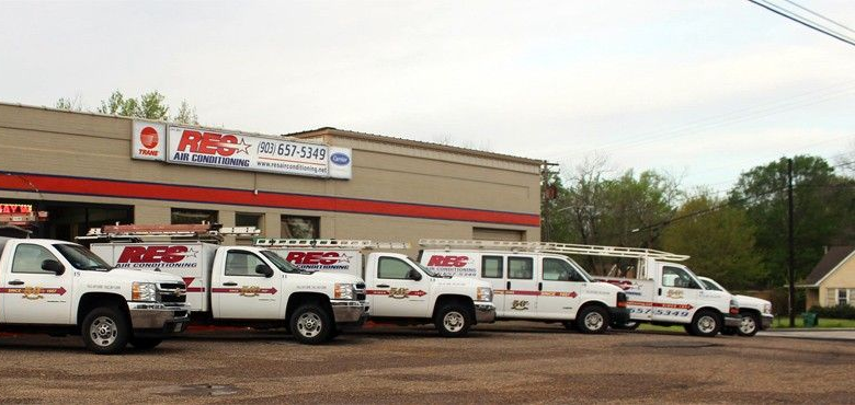 Row of white service trucks parked outside an APC building under a large sign