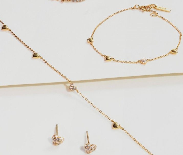 Gold jewelry set: necklace, bracelet, and earrings with heart-shaped charms and small diamonds, set against a white backdrop.