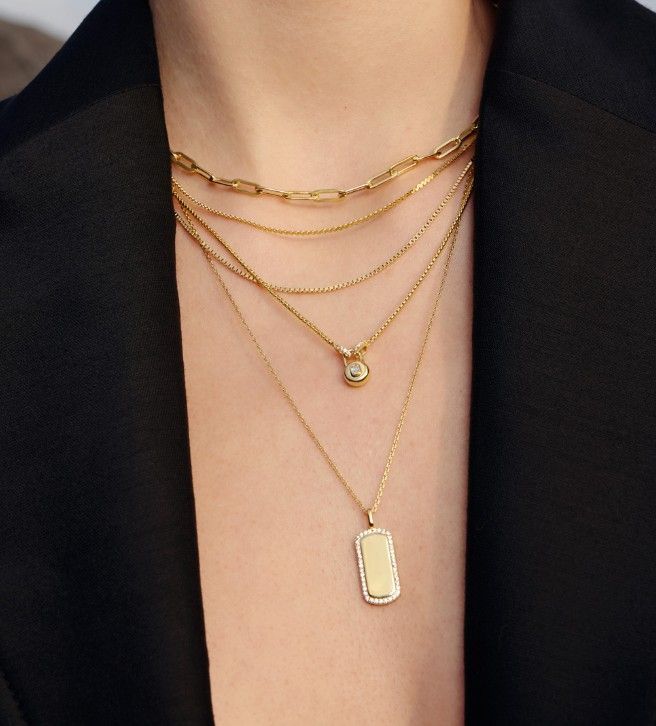 Woman wearing layered gold necklaces, over a black blazer.
