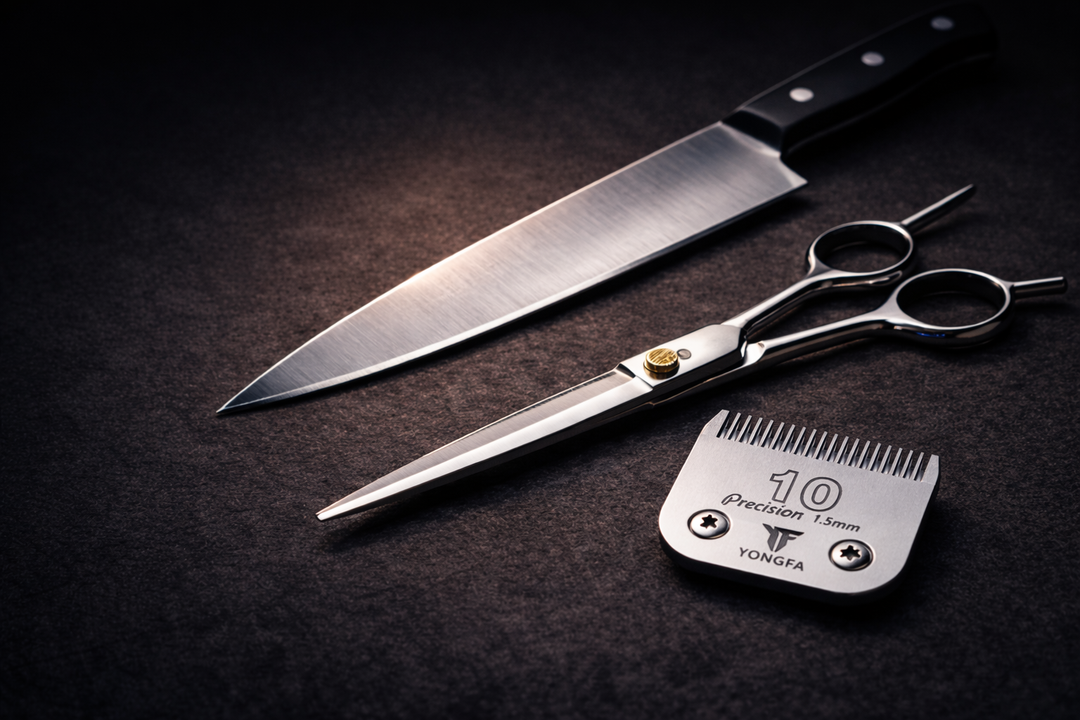 Knife, scissors, and a clipper blade arranged on a dark, textured surface.