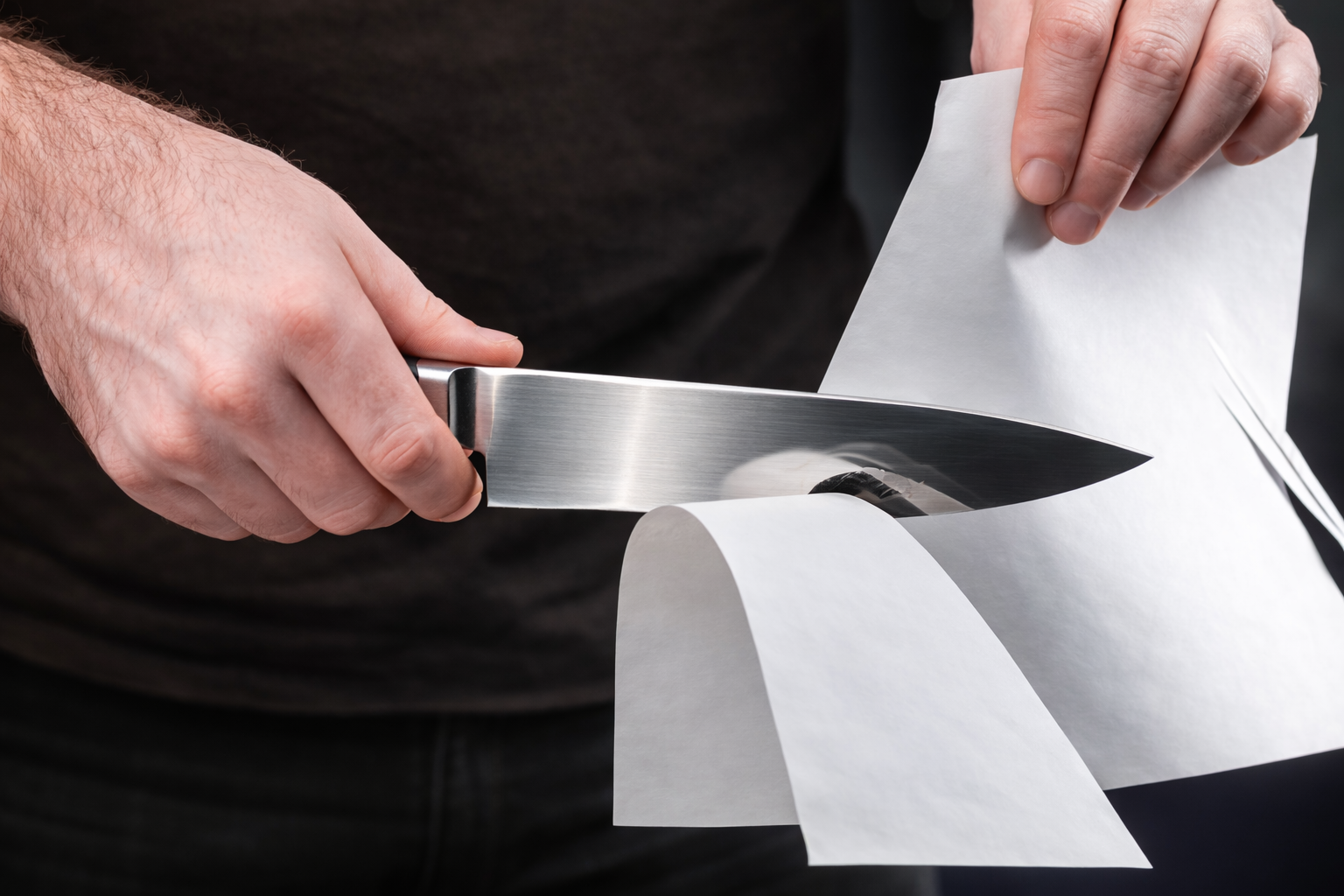 A person tests the sharpness of a knife by slicing through a piece of paper.