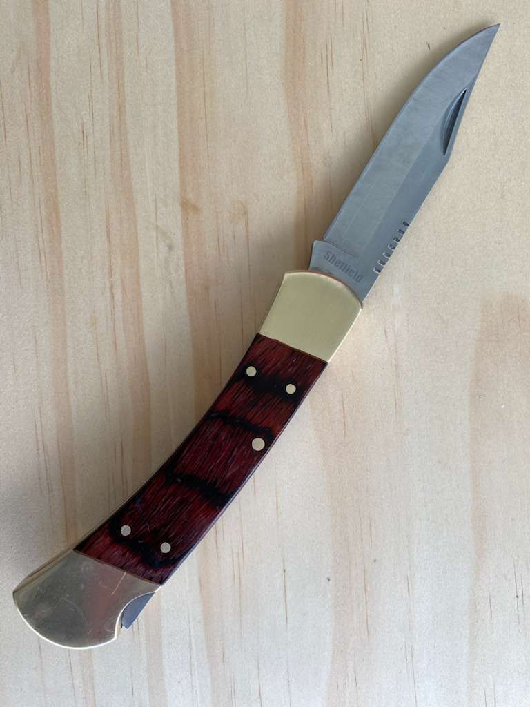 Pocketknife with wooden handle, brass bolsters, and partially serrated blade, on wood surface.
