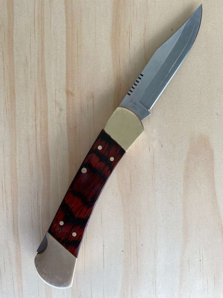 Pocket knife with a serrated blade, wooden handle, and brass bolsters, resting on wood.