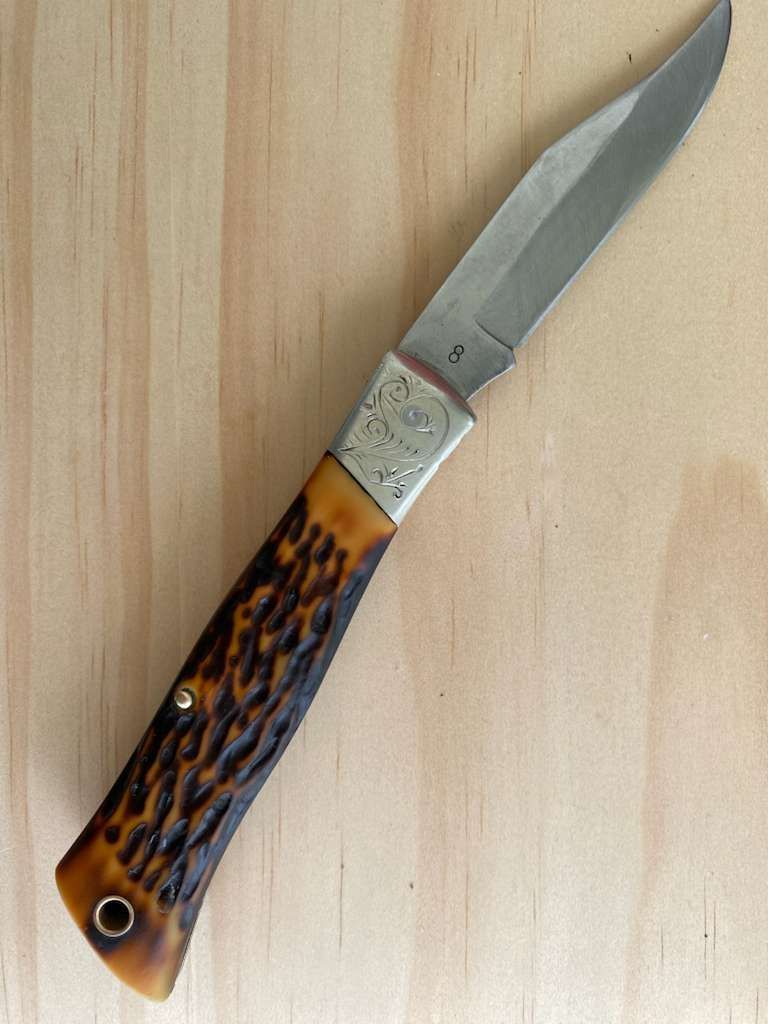 Pocket knife with antler-like handle, silver bolster, and partially open blade on a wood surface.