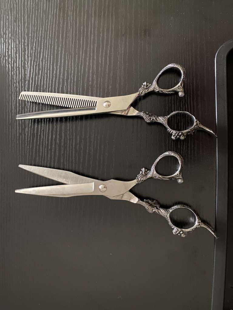 Two pairs of ornate silver hair cutting shears on a dark surface. One pair is thinning shears.