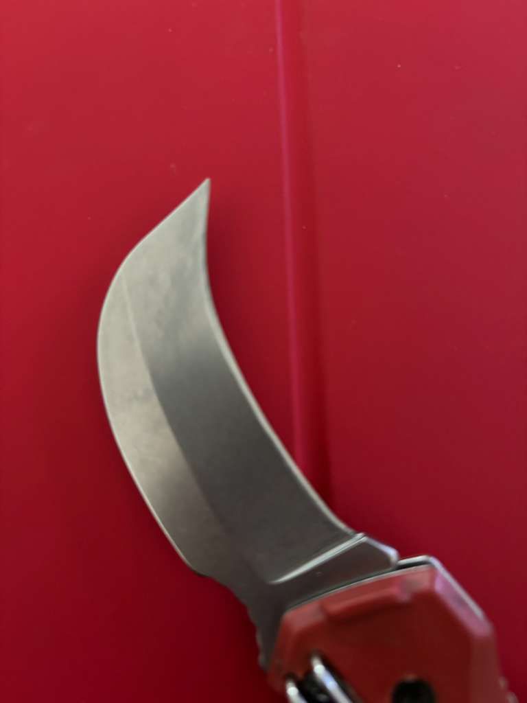 Curved blade knife with red handle against a solid red background.