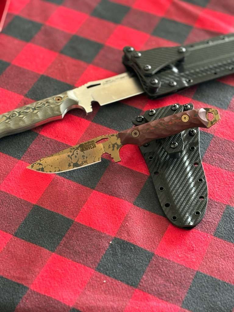 Two knives with sheaths on red and black plaid fabric.