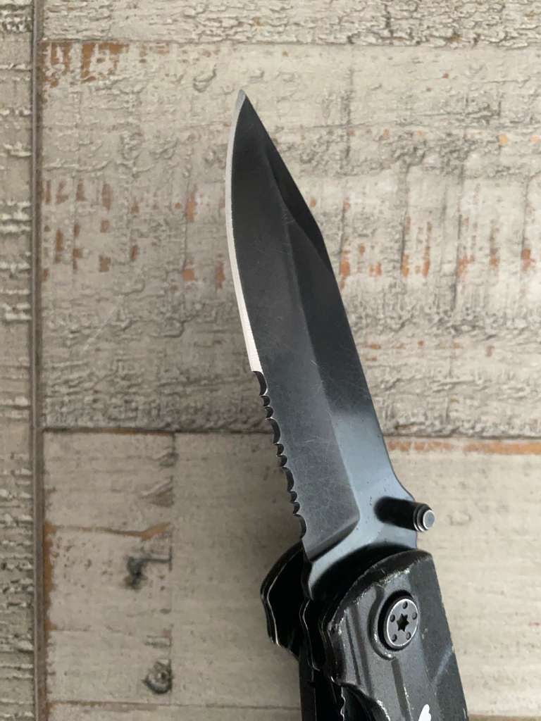 Black pocket knife with serrated edge, on a weathered wooden surface.