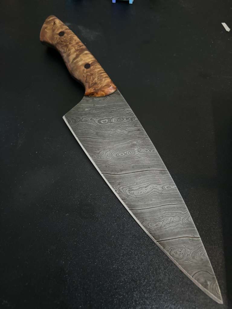 Chef knife with patterned blade and wood handle.