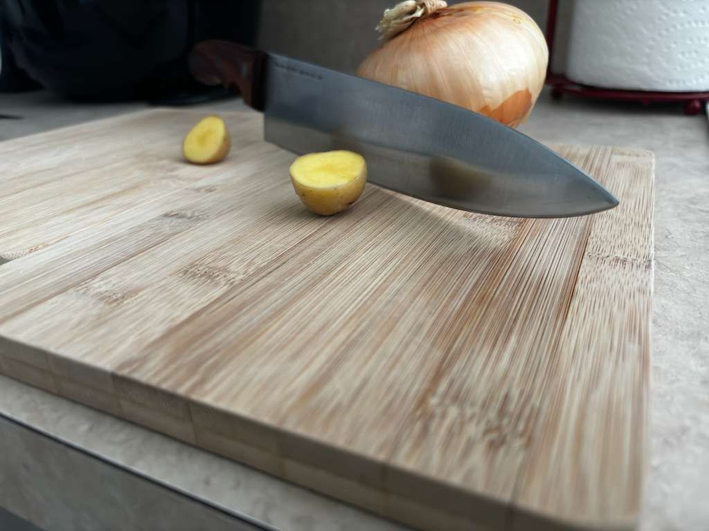 Cutting board with knife, onion, and two halved yellow potatoes.