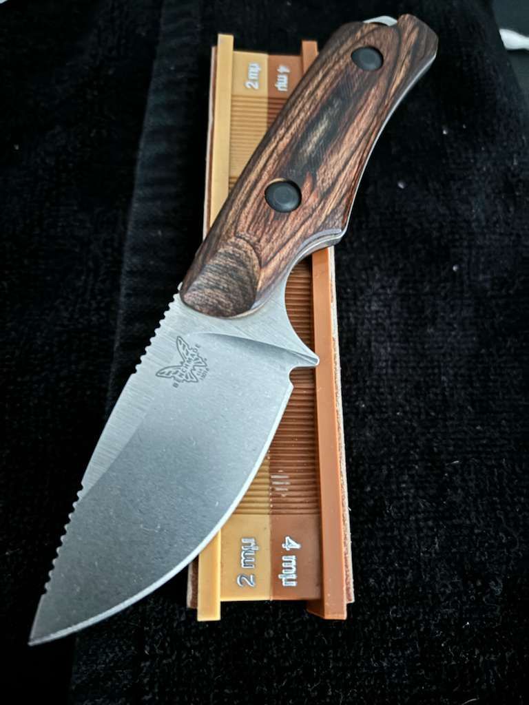 Knife with wooden handle, resting on a sharpening stone set against a black background.