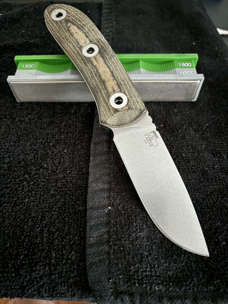 A fixed blade knife with a tan and black handle, atop a sharpening stone on a black surface.