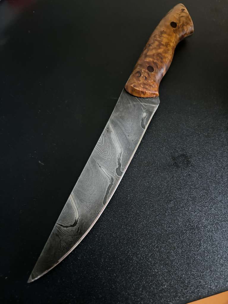 Damascus steel knife with a patterned blade and wooden handle on a dark surface.