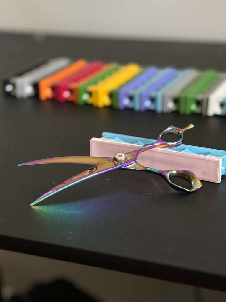 Iridescent scissors rest on a dark surface, with a row of colorful knife sharpeners in the blurred background.