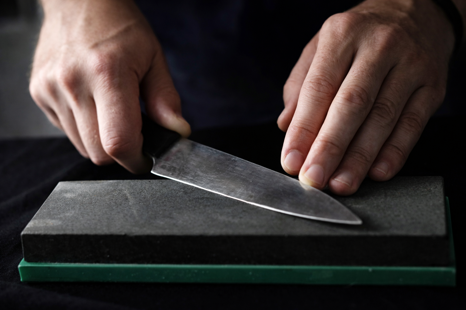 Hands sharpening a knife on a sharpening stone, with the blade at an angle.