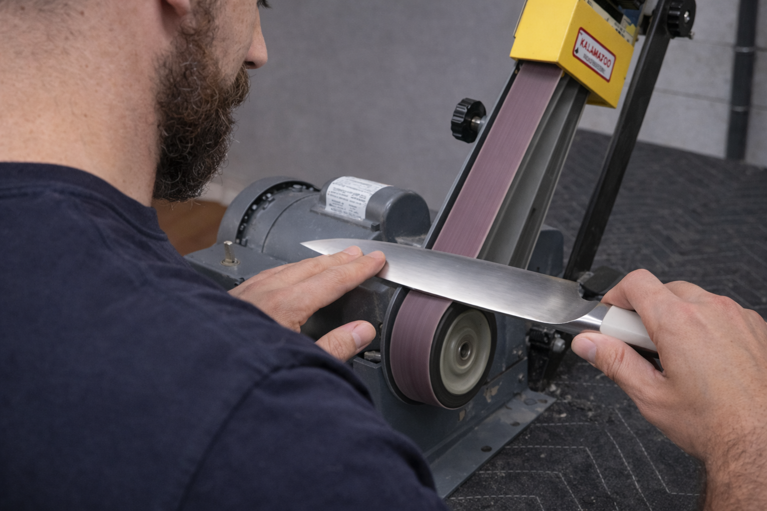 Man sharpening a knife on a belt sander; he's holding the blade against the moving belt.