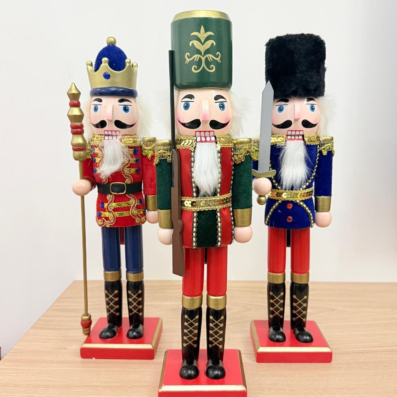 Tres cascanueces festivos de madera con uniformes rojos, verdes y azules, colocados sobre una mesa.