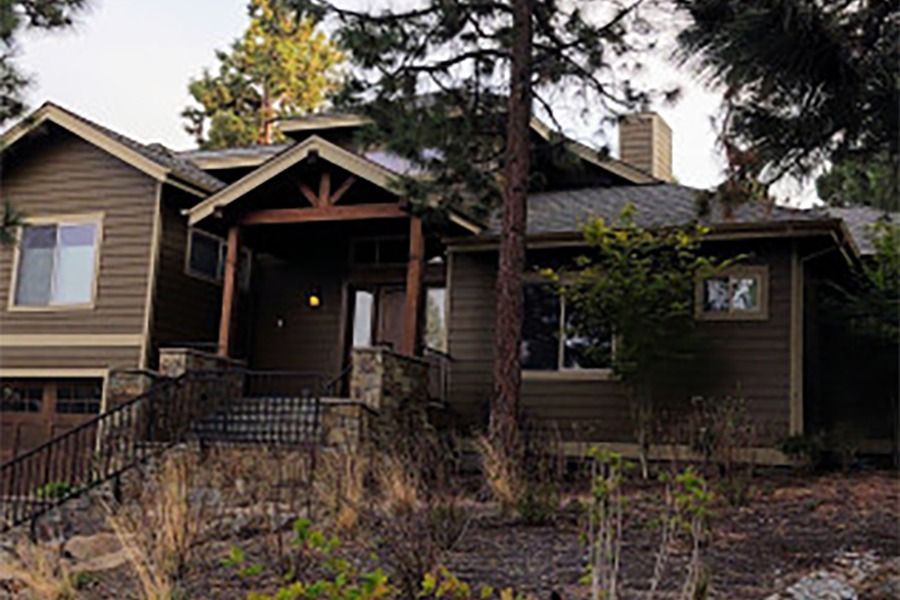Brown house with stone accents, covered entry, and sloped yard with sparse vegetation.