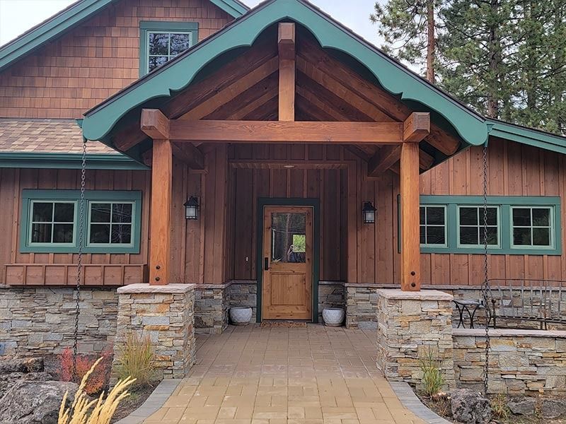 Brown wooden building with green trim, stone pillars, and a covered entrance.