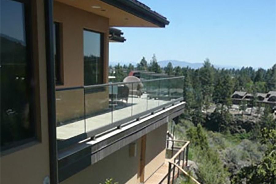 Balcony with glass railing, overlooking a scenic landscape of trees and mountains on a sunny day.
