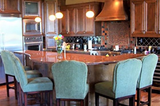 Kitchen with a wooden island, green chairs, and copper range hood.