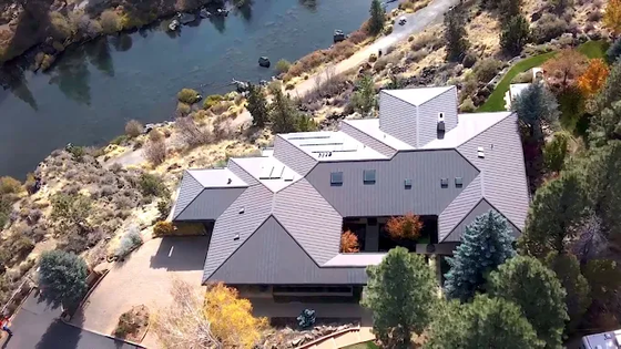 Aerial view of a modern house with gray roof beside a river and dry, rocky landscape