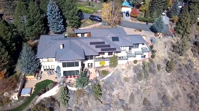 Aerial view of a large gray-roofed house surrounded by trees on a hillside.